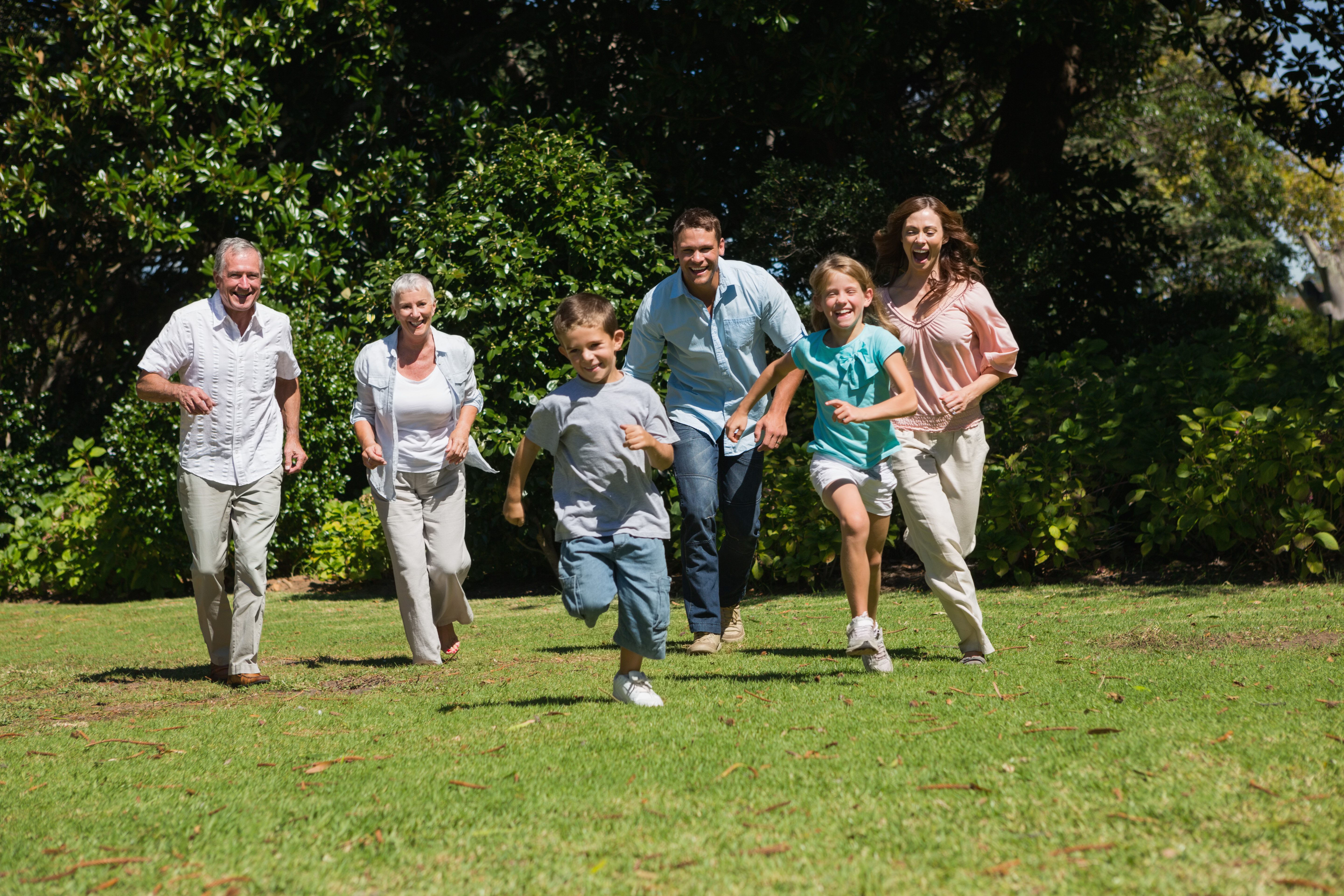 Happy multi generation family running towards camera in the park on su